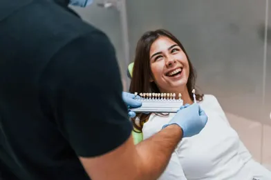 A cheerful woman smiling as her dentist shows her a tooth color matching strip.